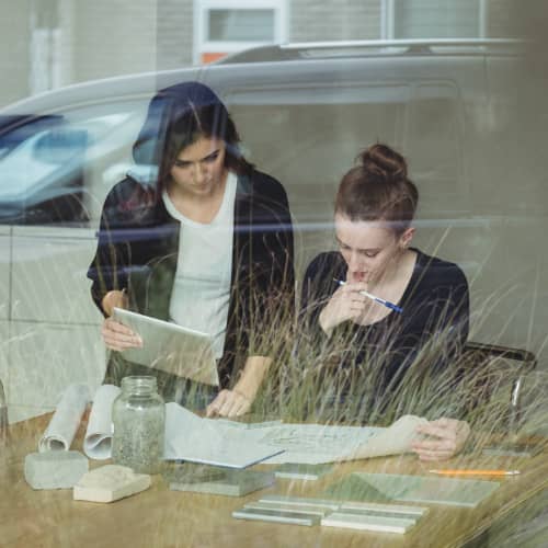 Deux femmes analysent un projet immobilier à travers une vitrine, illustrant la préparation stratégique d’une SCI avec l’aide d’un professionnel.